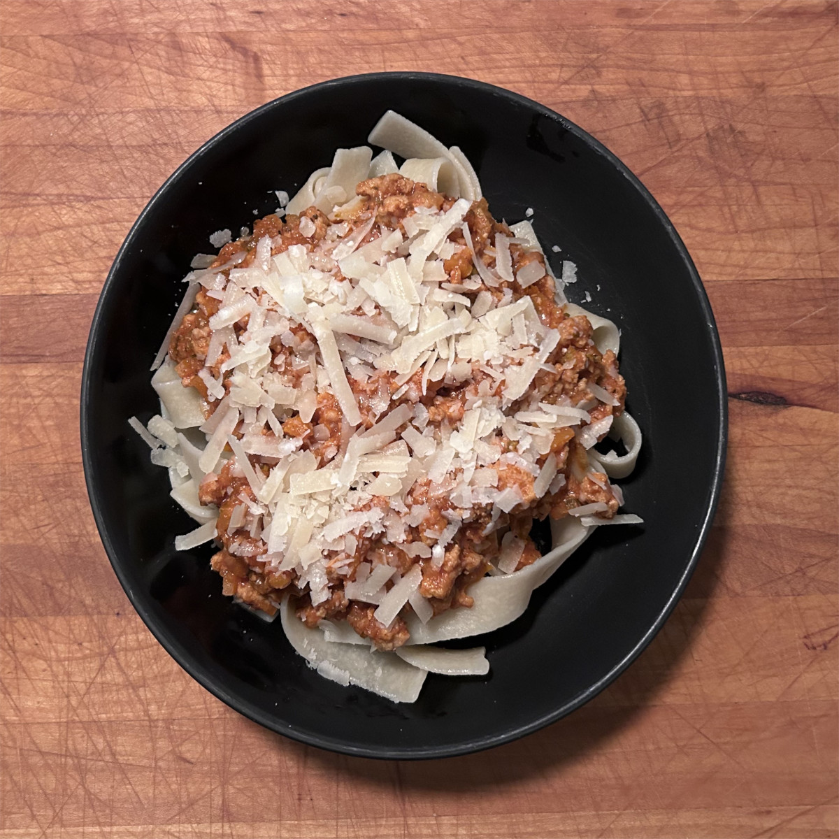 Chicken Bolognese with Pappardelle Pasta in black bowl and garnished with freshly grated Parmigiano Reggiano Cheese.